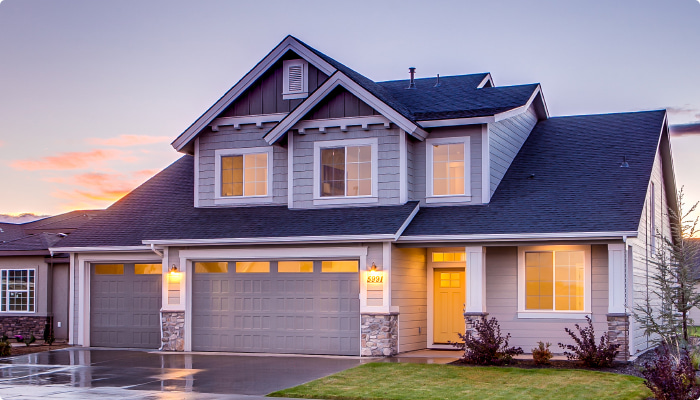 Two-story suburban house with warm glowing windows at sunset